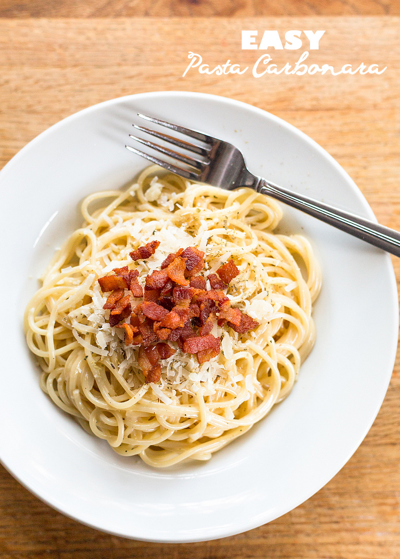 Spaghetti carbonara in a white bowl topped with bacon and cheese.