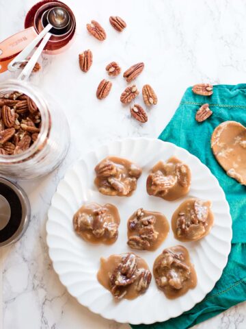 Pecan pralines on a white plate with pecans scattered on the surface.