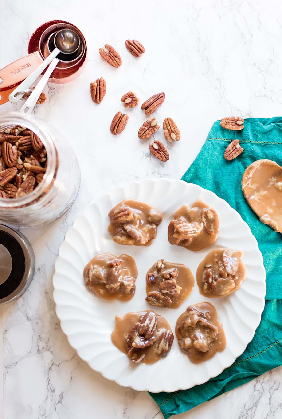 Pecan pralines on a white plate with pecans scattered on the surface.