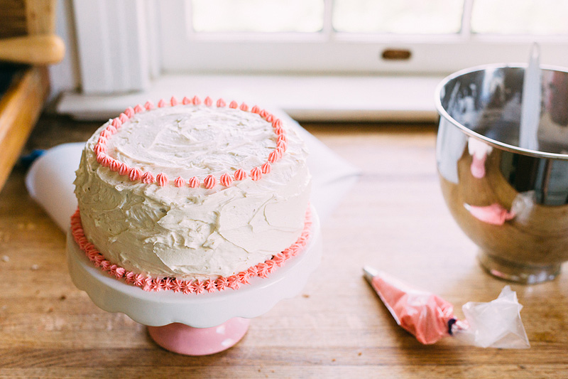 Piping pink frosting onto a birthday cake.