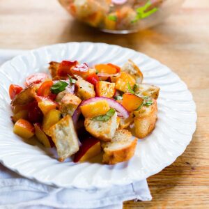 Peach panzanella on a white plate.