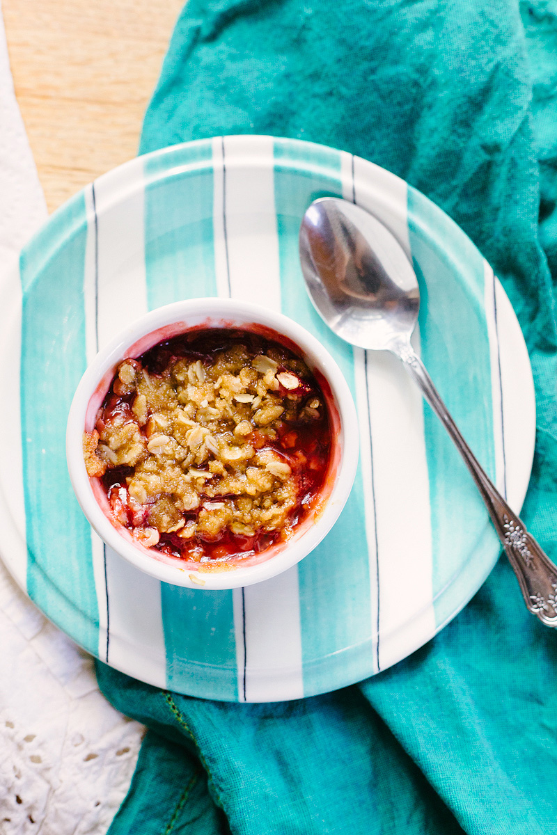 Cooked strawberry crumble in a ramekin on a teal and white plate.