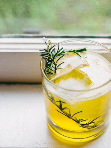 Bees knees cocktail in a class with a rosemary sprig for garnish