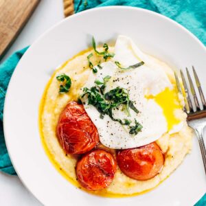 Breakfast polenta bowl topped with egg, tomatoes, and fresh basil.