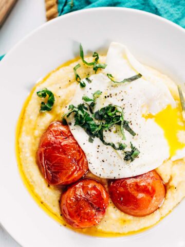 Breakfast polenta bowl topped with egg, tomatoes, and fresh basil.