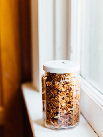 Cinnamon pecan granola in a glass jar sitting on a windowsill.