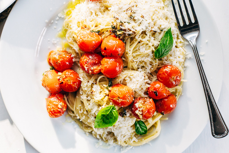 burst tomatoes served on spaghetti with fresh basil leaves and parmesan cheese