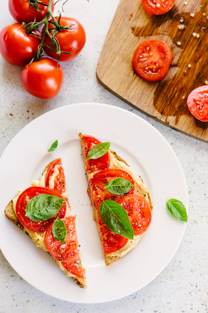 toast topped with tomatoes, hummus, and fresh basil leaves.