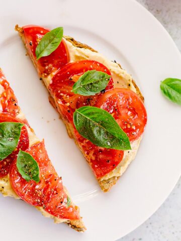 toast topped with hummus, tomatoes, and fresh basil leaves