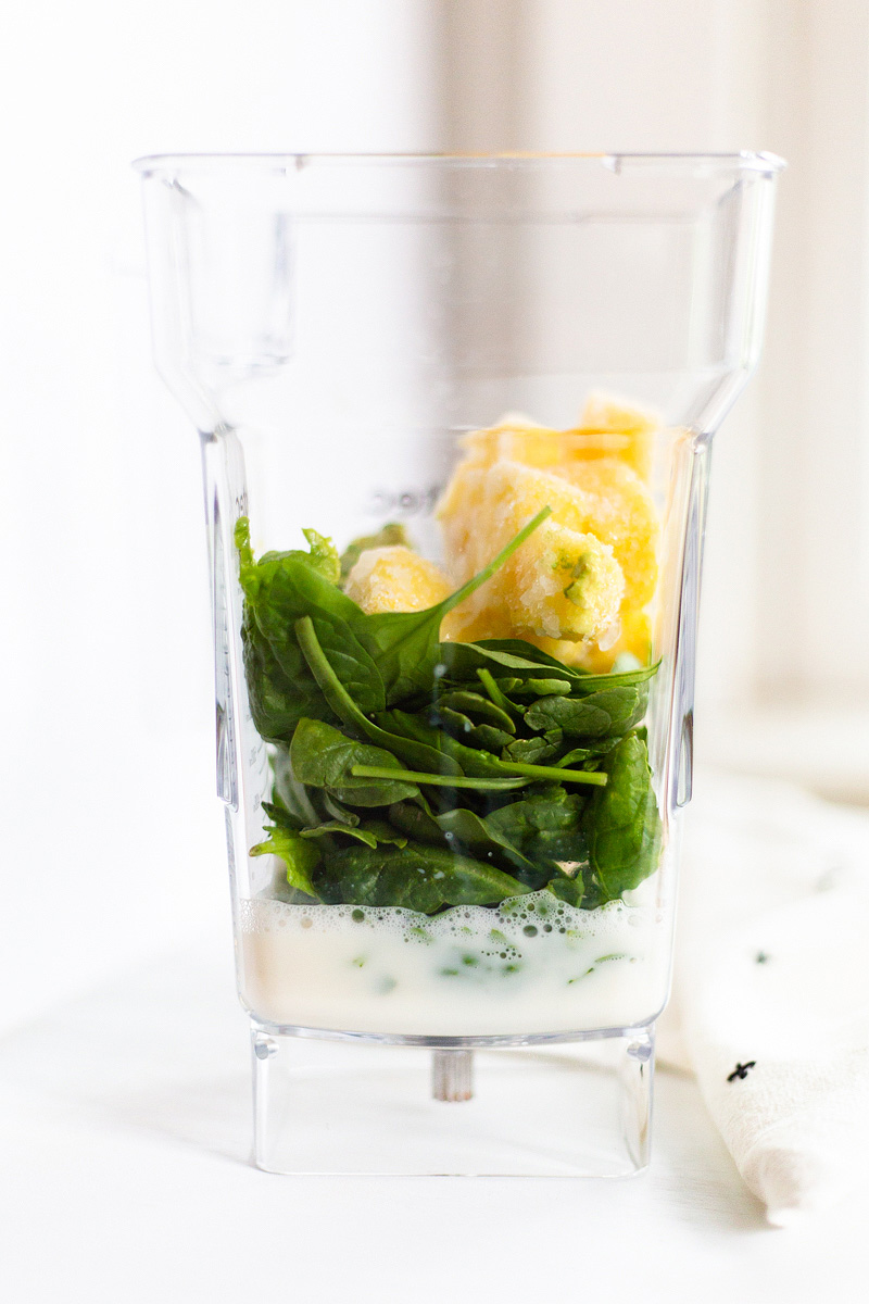 spinach, almond milk, and frozen pineapple in a smoothie jar.