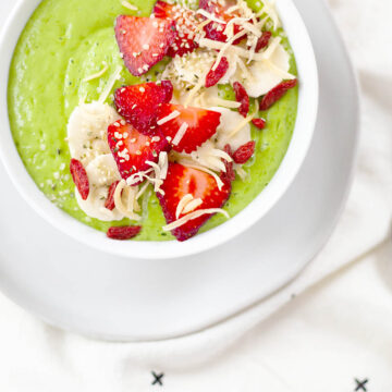 Creamy green smoothie bowl topped with sliced strawberries and bananas.