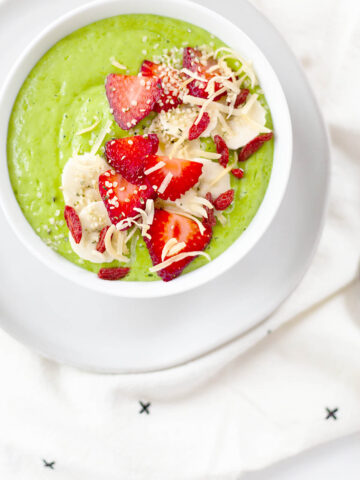 Creamy green smoothie bowl topped with sliced strawberries and bananas.