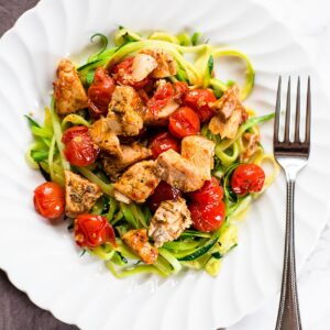 Zoodles with tomatoes and chicken on a white plate.