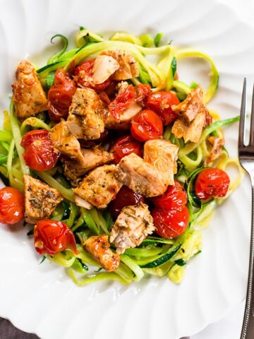 Zoodles with tomatoes and chicken on a white plate.