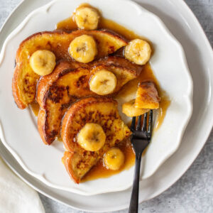 Bananas foster french toast on a white plate.