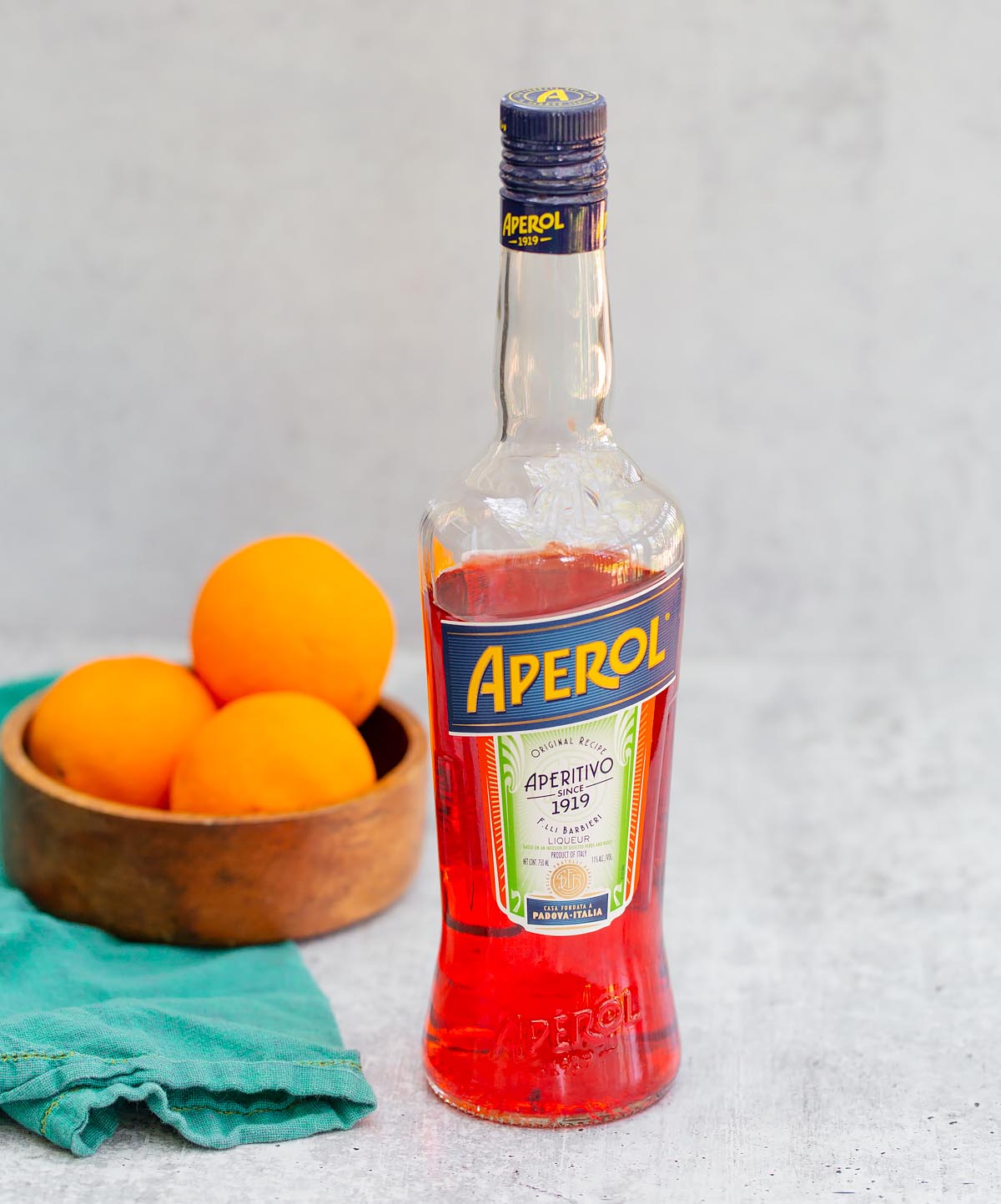 a bottle of aperol with a bowl of oranges in the background