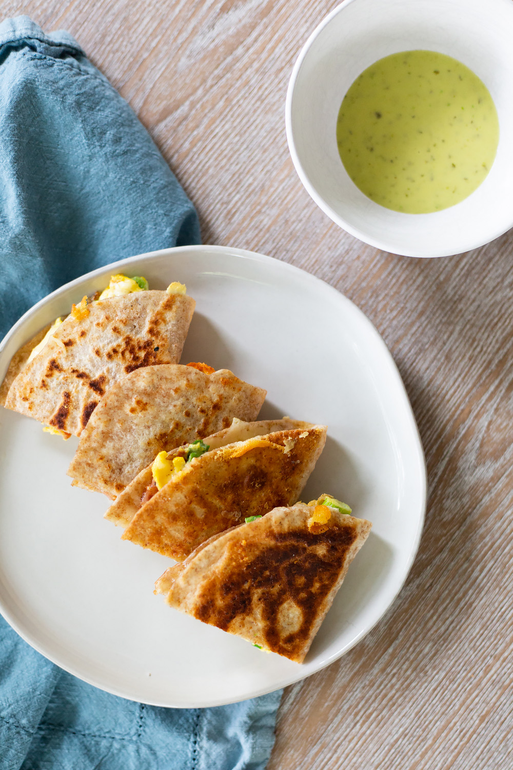 breakfast quesadilla on a plate with green salsa on the side.