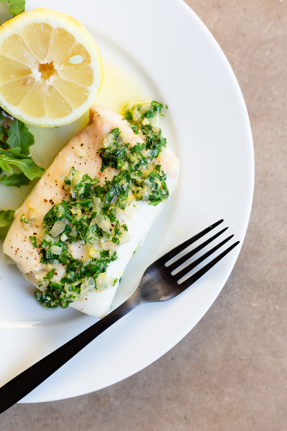 Cod with a Lemon Butter Shallot Sauce and a black fork.