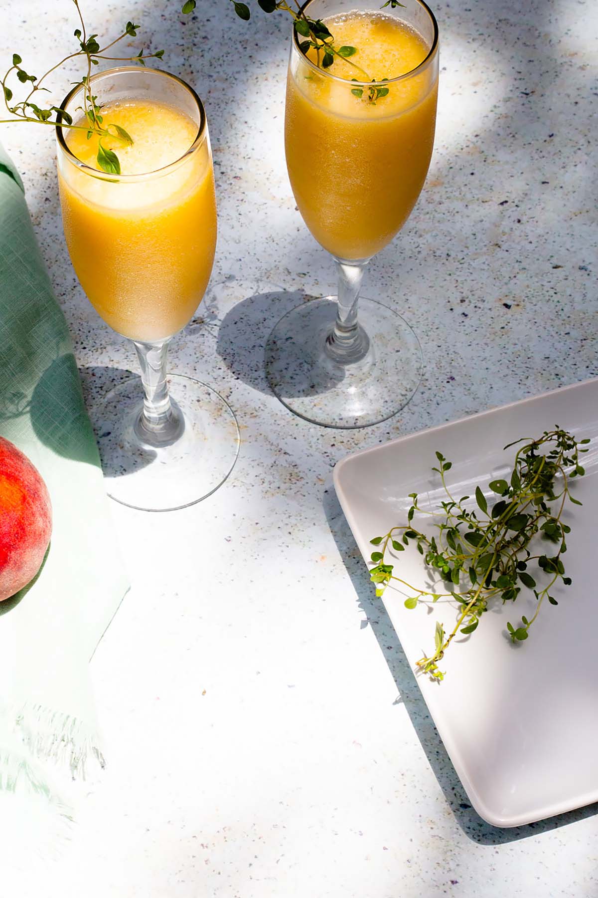 Two peach bellinis in glasses with thyme on the side.