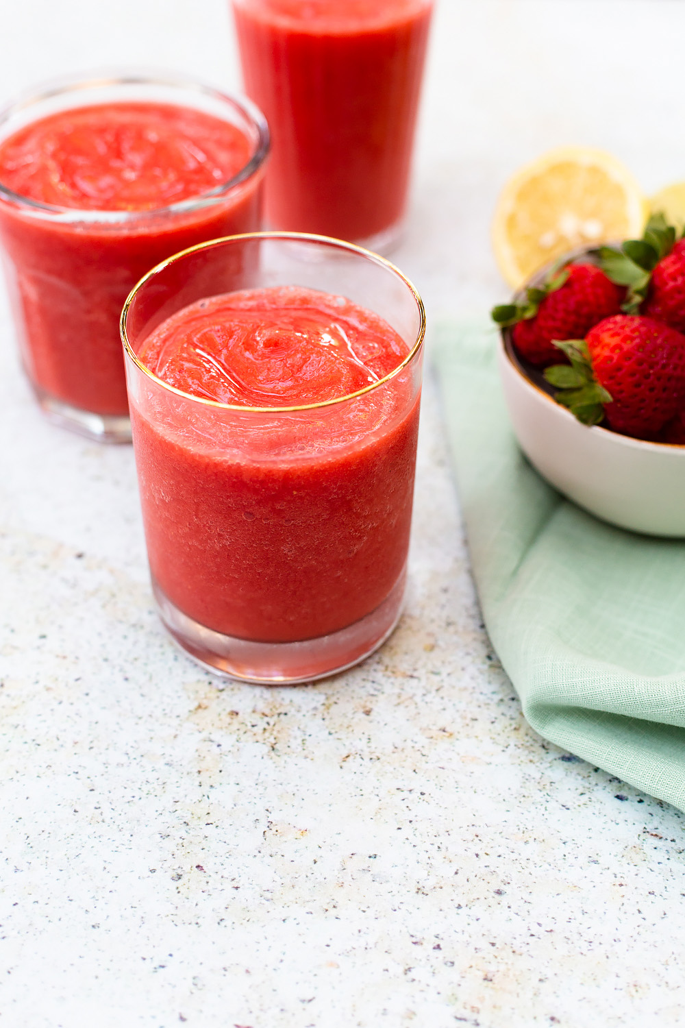 Three strawberry slushies with a side of fresh strawberries.