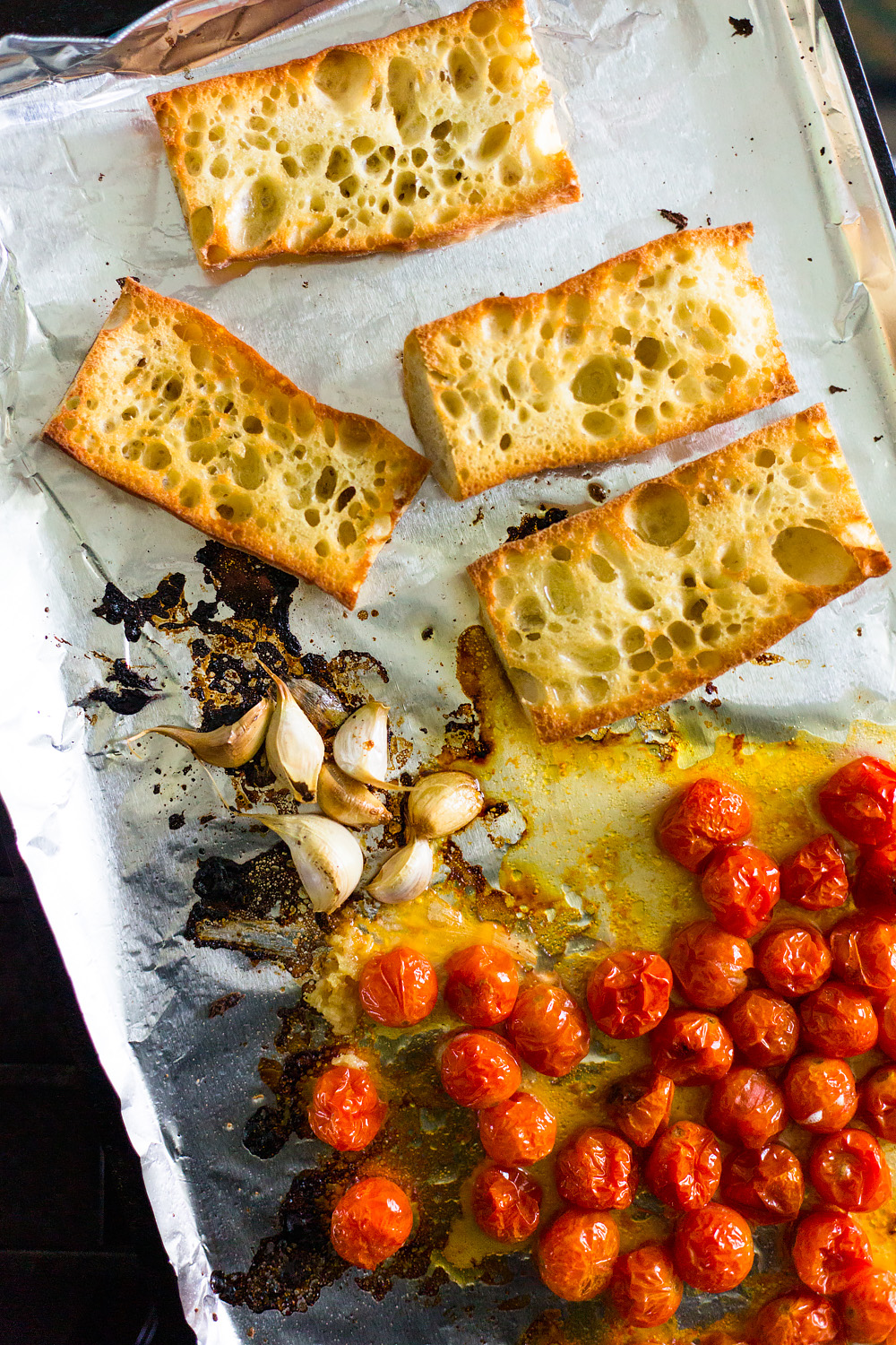 toasted bread, roasted garlic, and roasted tomatoes on a baking sheet.
