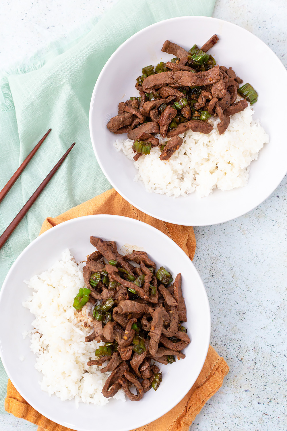 two bowls of steak and shishito peppers served with rice.