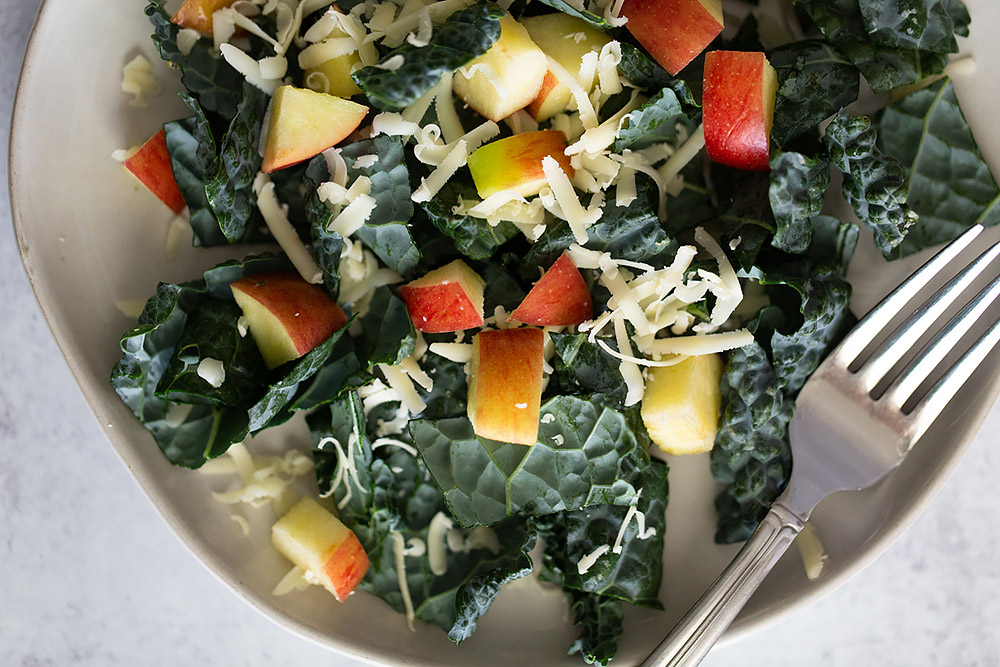 tuscan kale salad with apples and cheese with a fork.