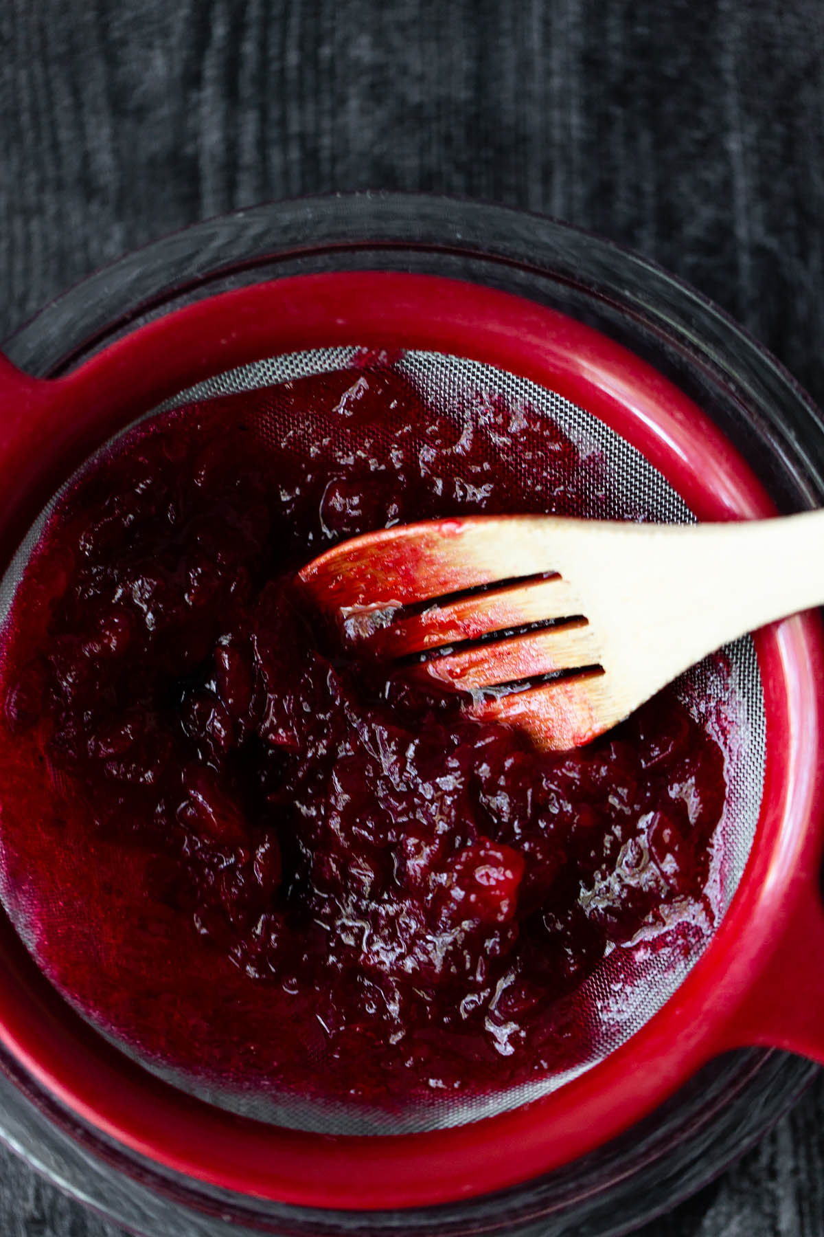 pushing cooked cranberries through a mesh strainer