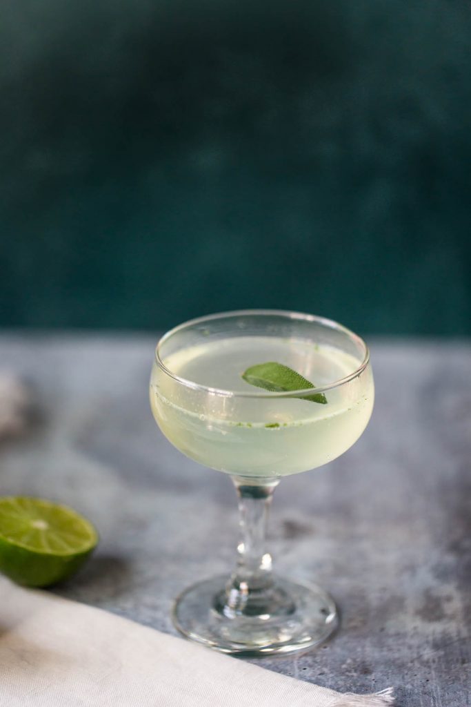 sage lime mocktail topped with a sage leaf in a coupe glass