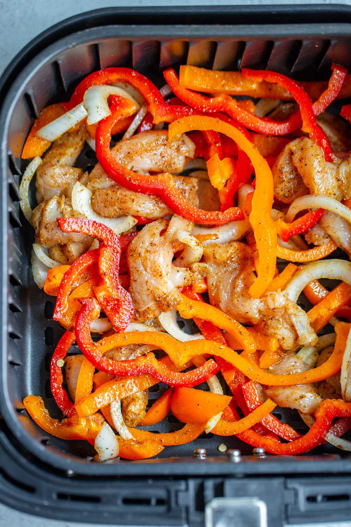 Uncooked chicken fajitas in air fryer basket