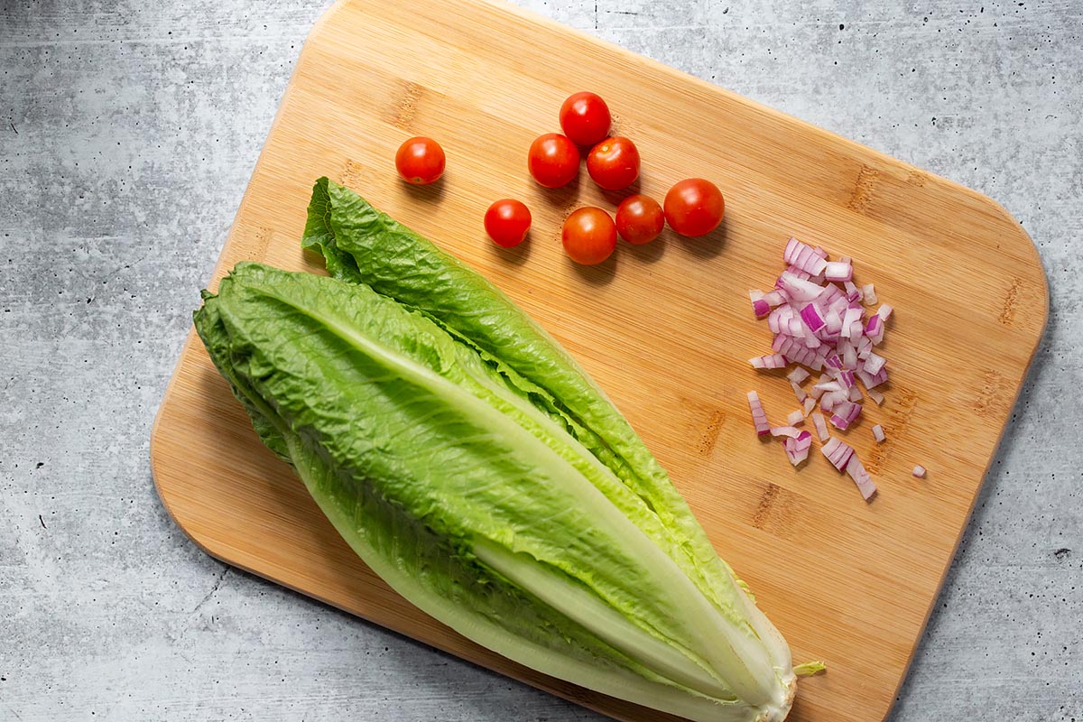 romaine lettuce, cherry tomatoes, and chopped red onion on a cutting board