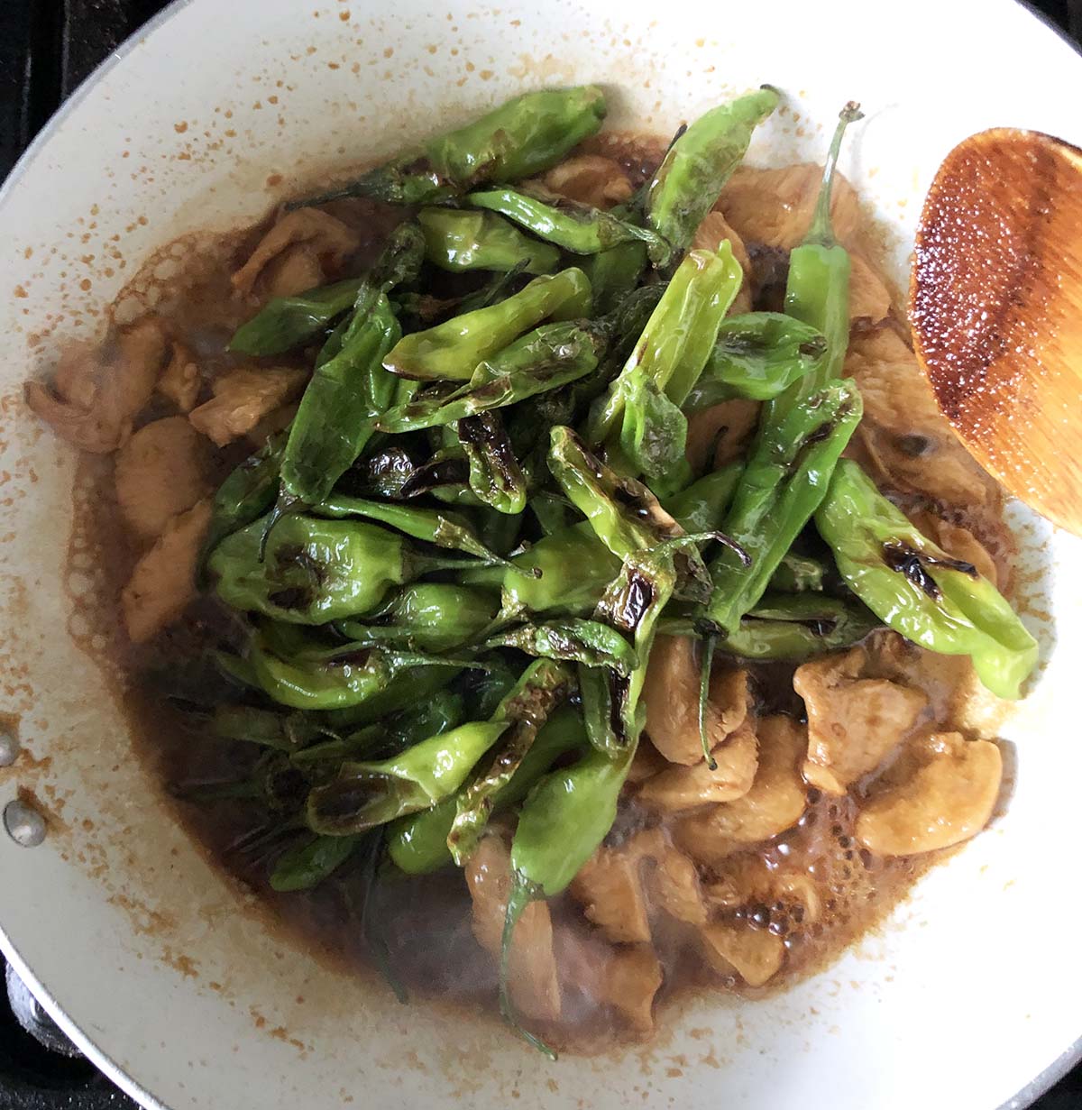 chicken and shishito peppers cooking in a skillet