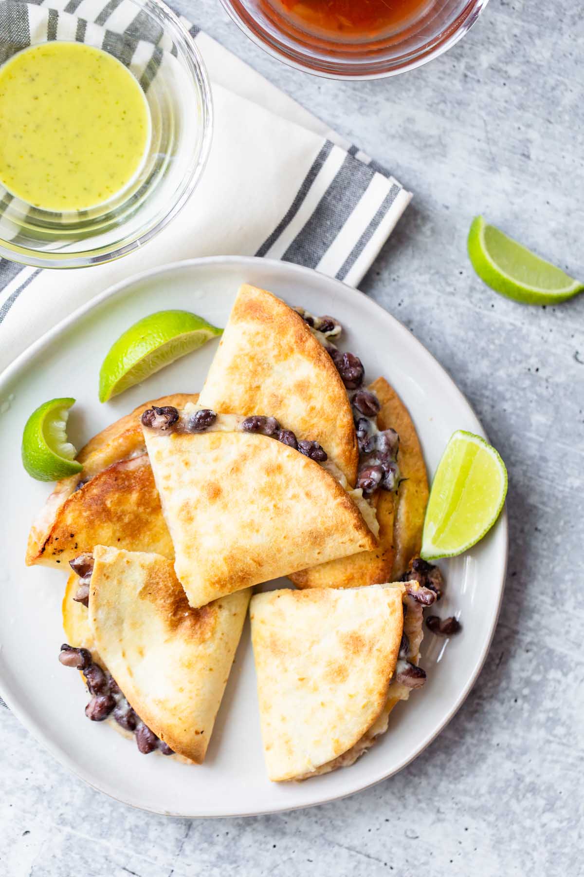 quesadillas on a plate with lime wedges and salsas on the side