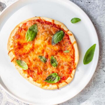 air fried tortilla pizza on a white plate with basil leaves