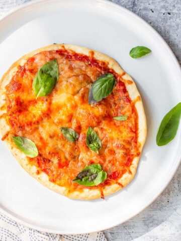 air fried tortilla pizza on a white plate with basil leaves
