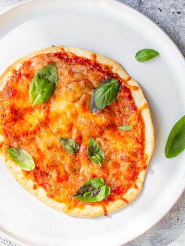 Air fryer tortilla pizza on a white plate topped with basil leaves.