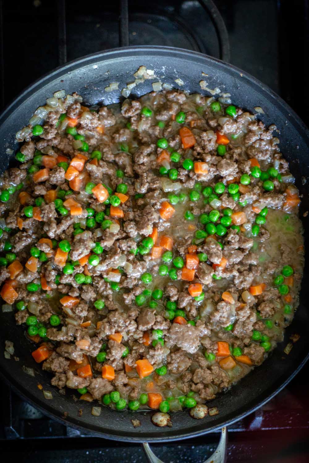 meat, peas, and carrots cooking in a skillet