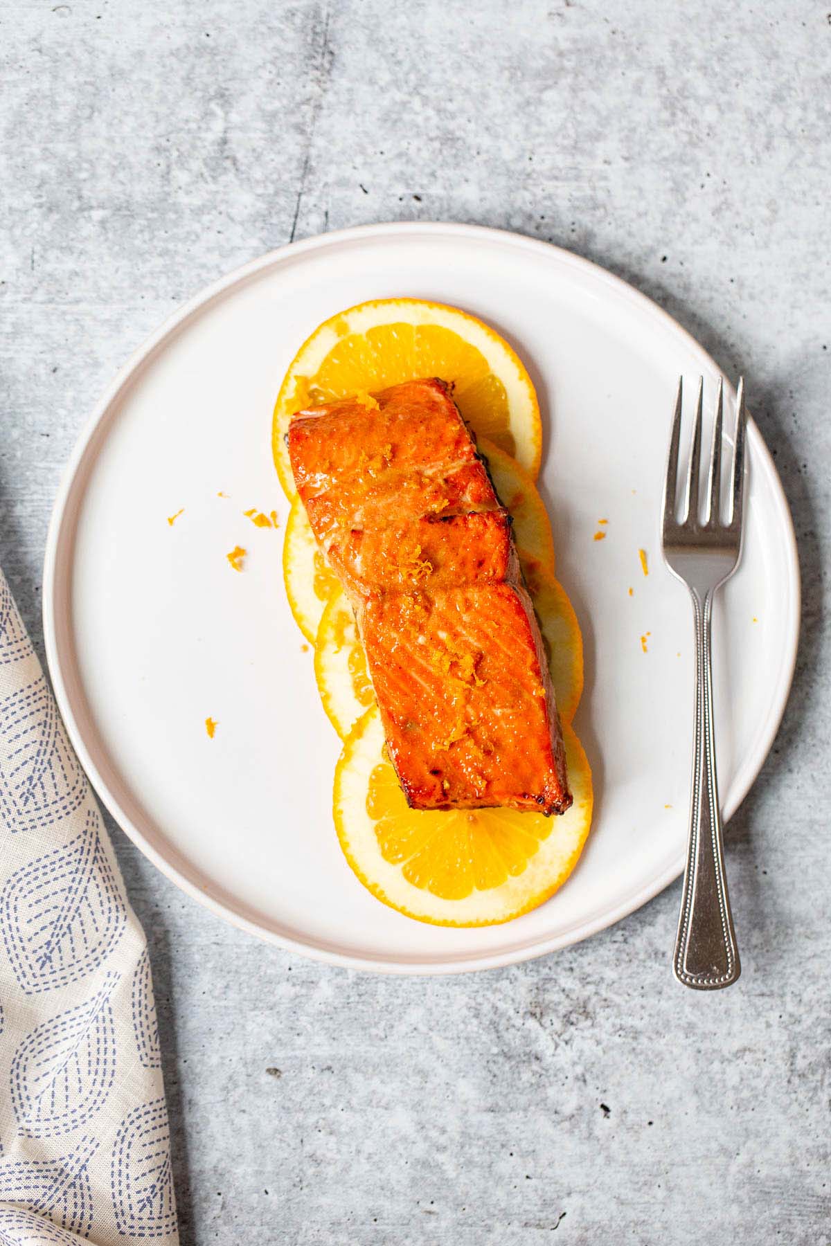 salmon on orange slices on a white plate with a fork