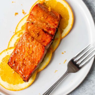 salmon on orange slices on a white plate with a fork