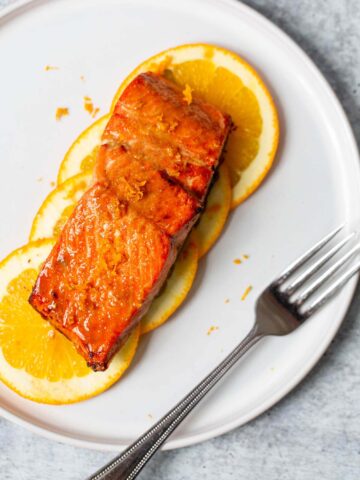 salmon on orange slices on a white plate with a fork