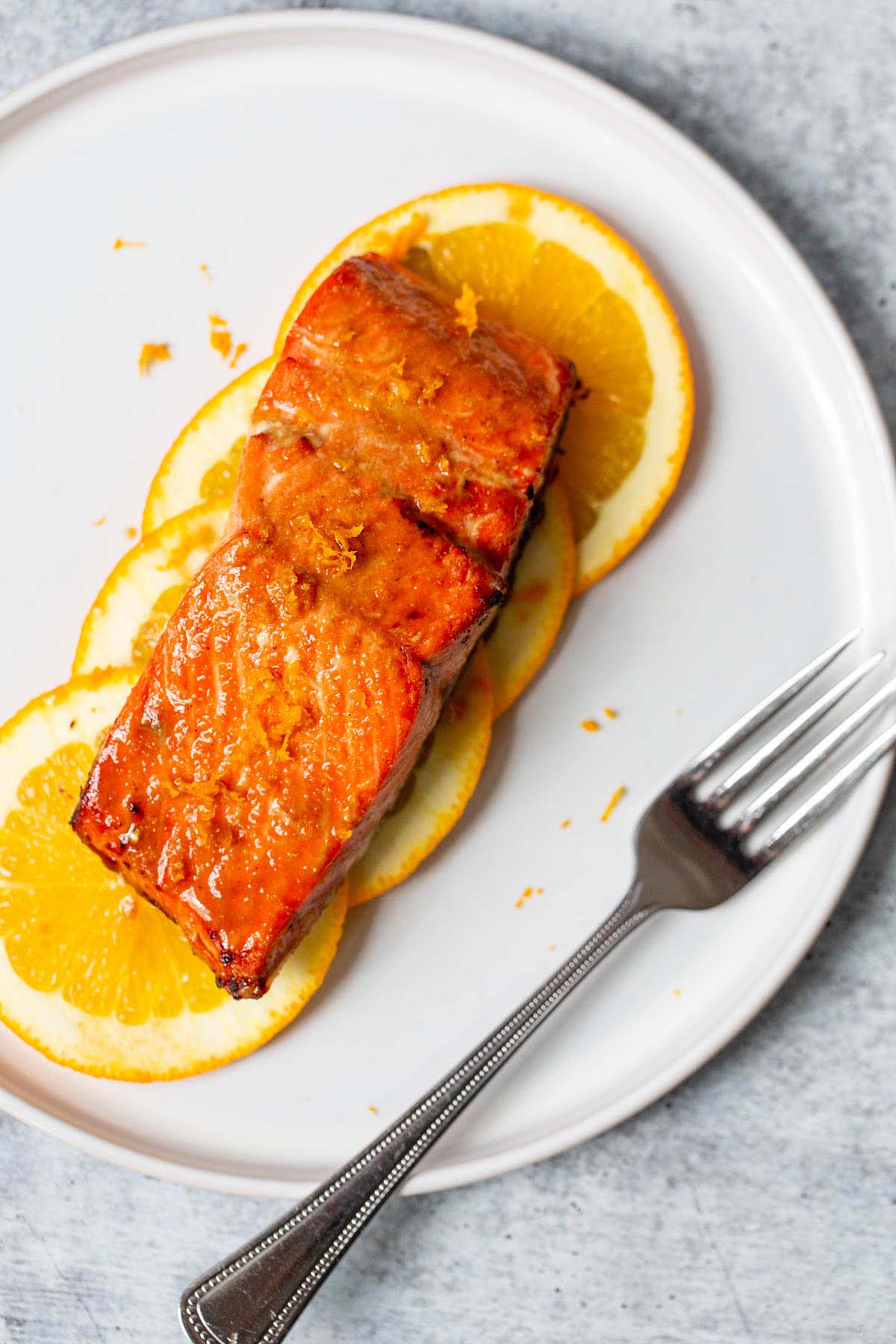 salmon on orange slices on a white plate with a fork