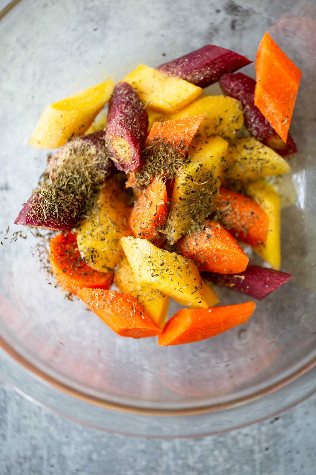 Sliced rainbow carrots in a bowl with dried herbs.