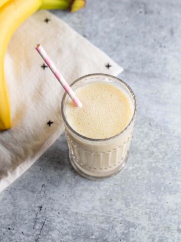 Smoothie in a glass with a pink and white straw.