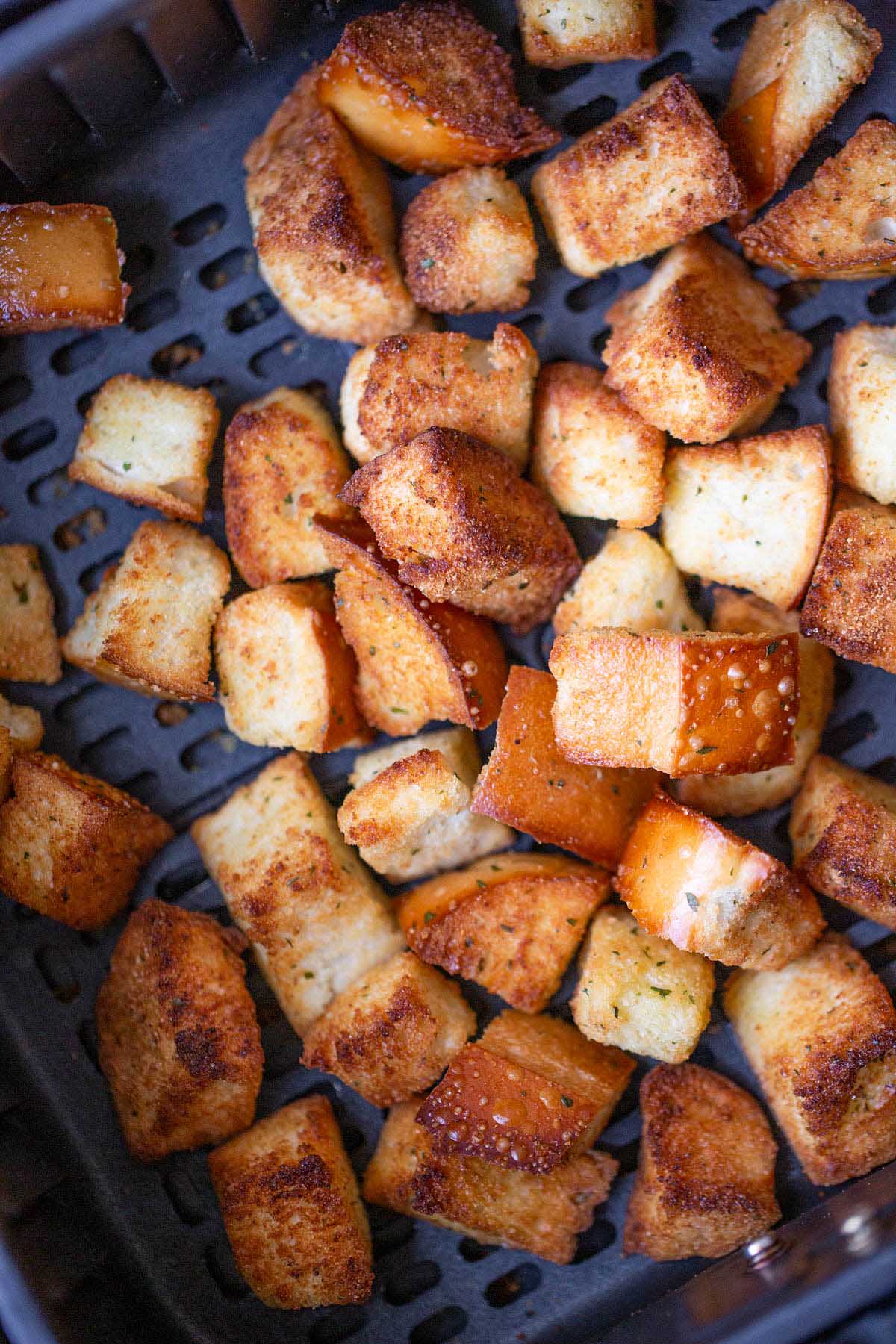 Cooked croutons in air fryer basket.