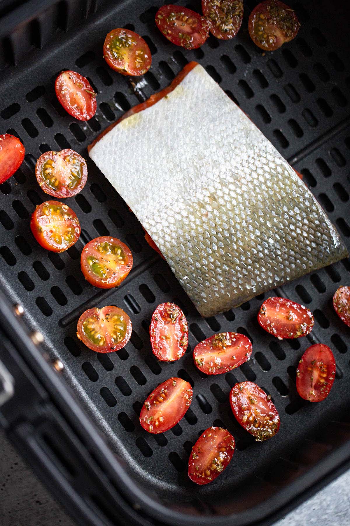 Salmon and tomatoes in an air fryer basket.