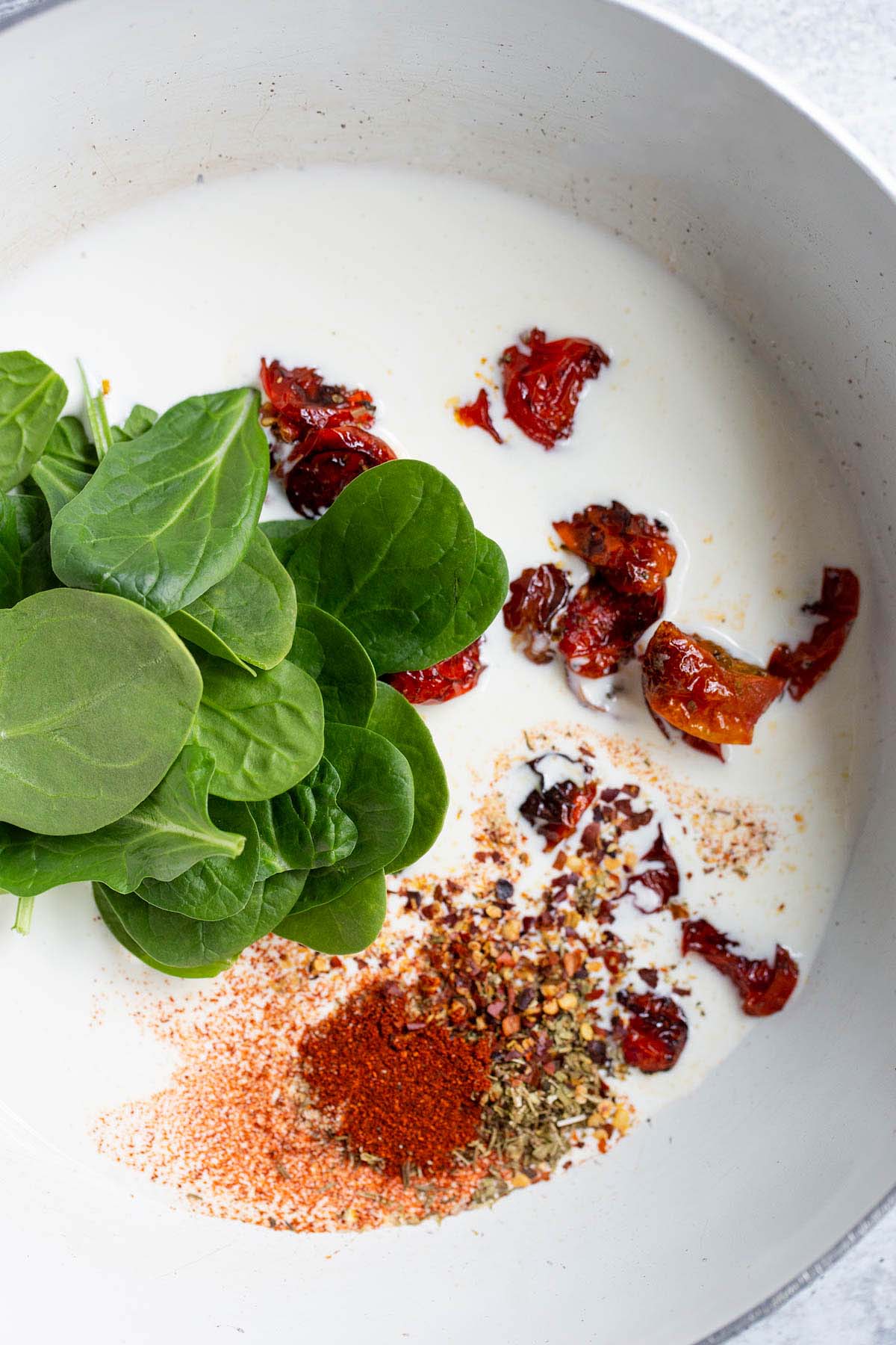 Spinach. tomatoes, spice, and cream in a skillet.