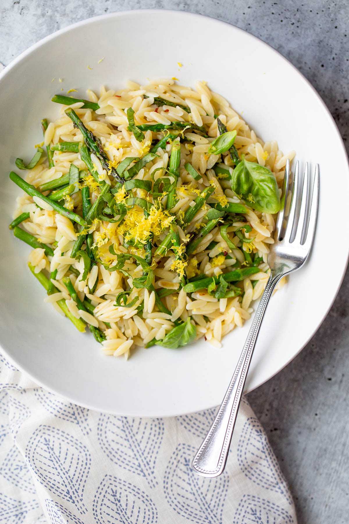 Orzo and asparagus in a bowl topped with lemon zest.