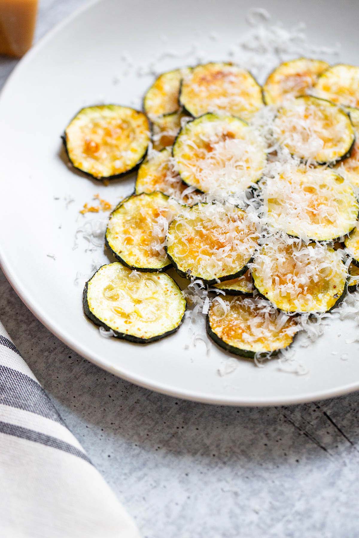 Zucchini chips on a plate with parmesan cheese.