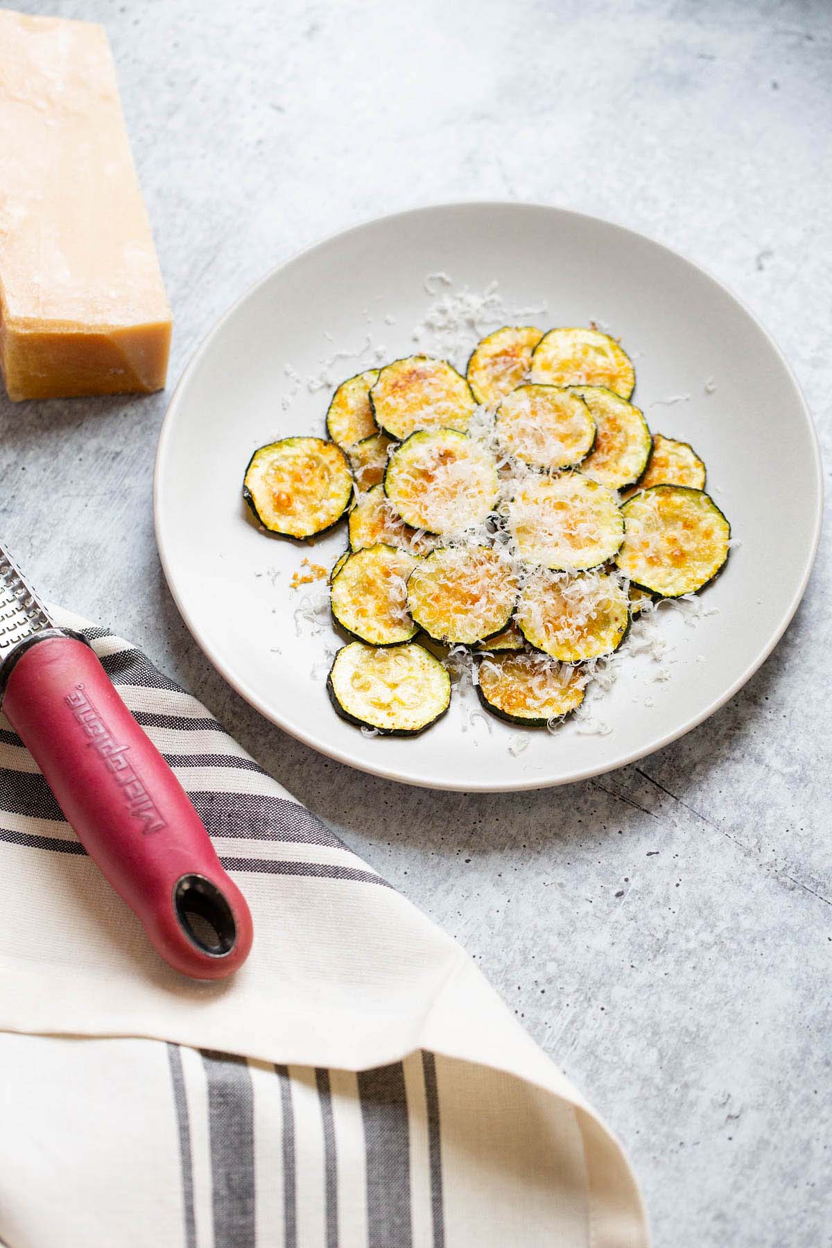 Zucchini on a plate with parmesan cheese on the side.