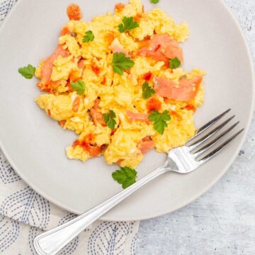 Scrambled eggs and smoked salmon on a plate with a fork.